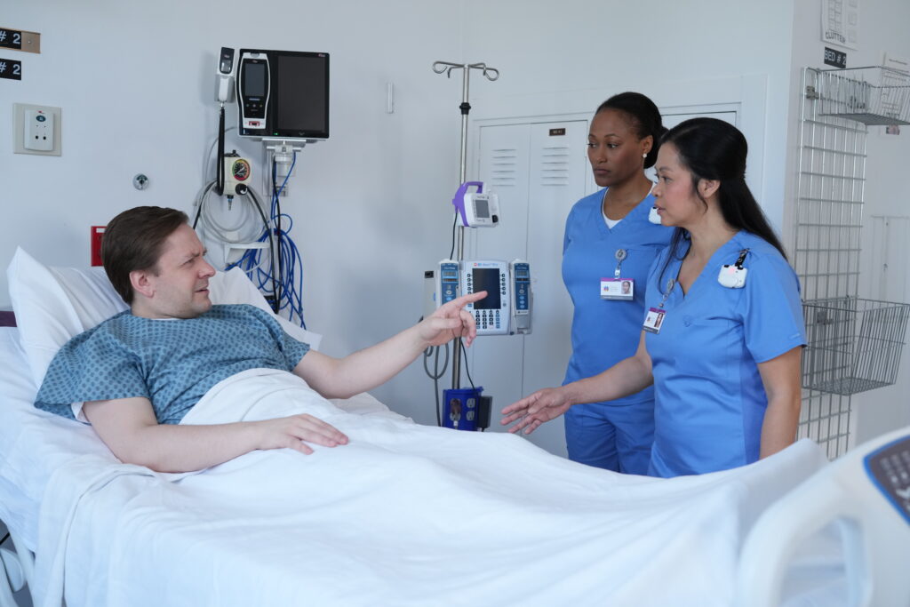 Patient speaking with two nurses in a hospital room while healthcare staff wear BioVigil hand hygiene monitoring badges